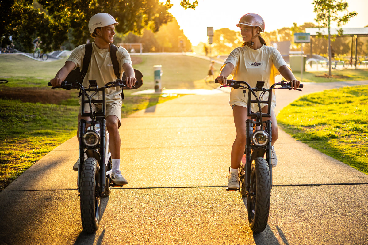 Two helmeted riders enjoying a sunny path on Sun Chaser electric bikes